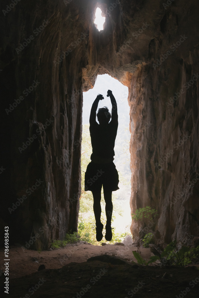 A silhouette of a man jumps in the entrance to a cave