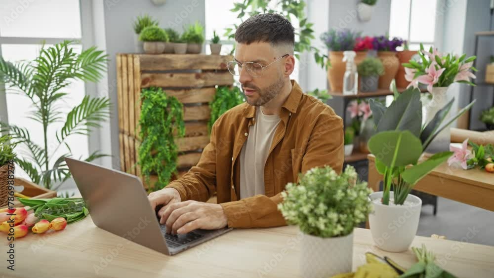 Hispanic man with glasses, working on laptop in a flower shop filled with plants and tulips. Hispanic man with glasses, working on laptop in a flower shop filled with plants and tulips.