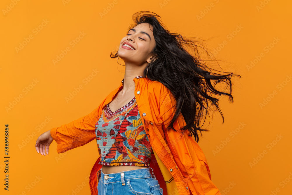 An enthusiastic Indian woman dances with cheerful moves to music against a bright orange backdrop.
