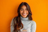 An enthusiastic Latina woman, in her late 20s, smiles warmly as she recommends a smartphone app on a vibrant orange background, demonstrating her tech expertise and engaging communication style.