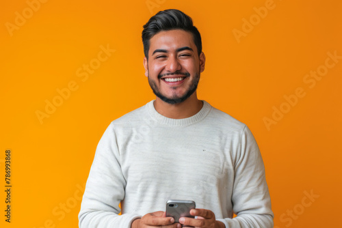 An enthusiastic Latina man, in his late 20s, smiles warmly as he recommends a smartphone app on a vibrant orange background, showcasing his engaging personality and persuasive abilities.