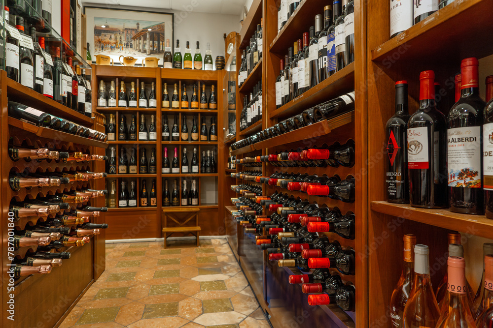Interior and hallway of a luxurious liquor store, wines, champagne, brandies and cognac, displayed, aligned and stacked on well-lit wooden shelves and bottle racks.