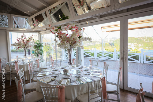 The elegant wedding table ready for guests. Decorated white wedding table for a festive dinner with pink flowers.