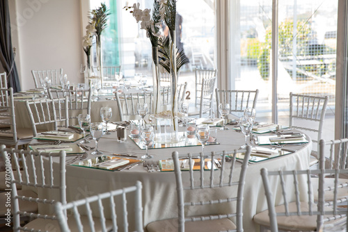 A beautifully decorated wedding reception venue with round tables adorned with white linens, mirrored centerpieces, and tall floral arrangements, creating an elegant and sophisticated atmosphere