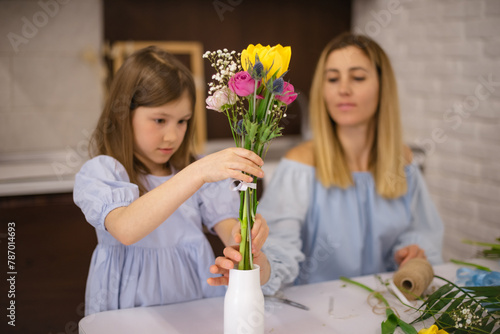 Girl put ready flower bouquet in vase. Mother and daughter making flower bouquet together
