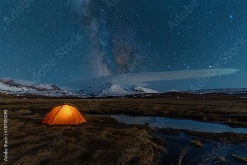 Illuminated orange tent under a starry sky in a snowy mountain landscape