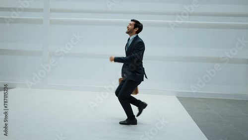 Project manager dancing to celebrate success project while moving to lively music with white background. Skilled business man holding bag while dancing with white background. Copy space. Exultant.