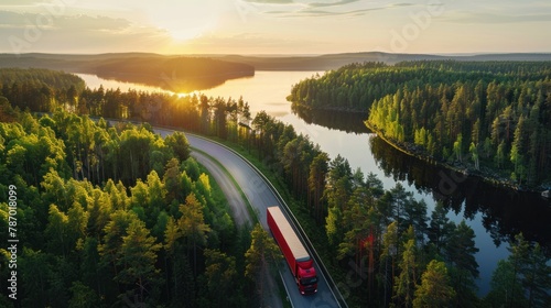 Aerial view of semi truck with cargo trailer on road curve at lake shore with green pine forest. Transportation background. Beautiful nature landscape at sunset in Republic of Karelia, Russia photo