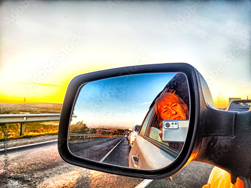 The side mirror of the car and the sun with bright rays behind it and the track on a trip in nature photo