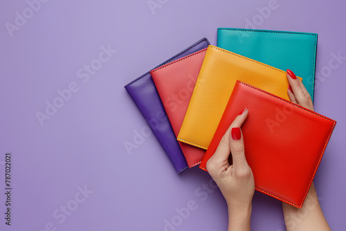 Colourful bags purses on purple background. Woman hand with red manicured nails holding wallet 