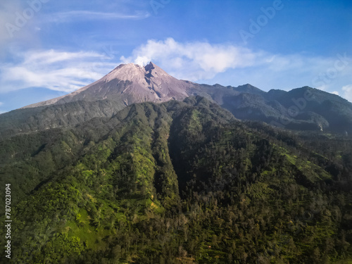 Aerial view of Merapi Volcano mountain covered by mist and fog in the morning with forest and hills below in Cangkringan, Sleman, Yogyakarta, Indonesia.