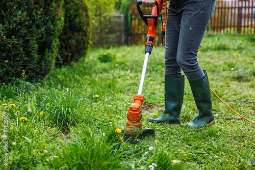 Woman cutting grass at backyard. Electric grass trimmer. Lawn care and spring gardening photo