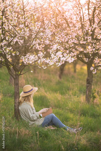 Writer looks for inspiration to write her book while contemplating in spring blooming orchard. Woman writing in notebook