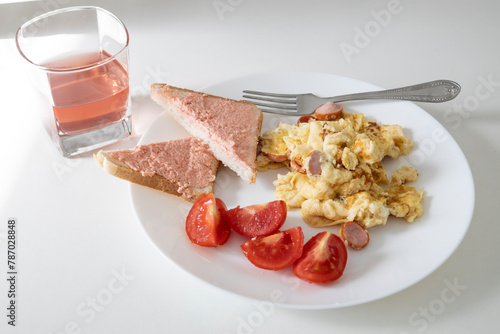 Delicious food - omelette with sausage, tomato slices, slices of bread with capelin caviar on a white plate and drink in glass