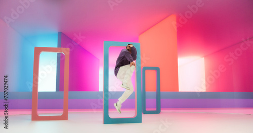 Young And Athletic Caucasian B-Boy Breakdancing To Break Beats in a Colorful Abstract Neon Lit Studio. Energetic Fashionable Male Dancer Talentedly Performing His Choreography On Multicolored Set. photo