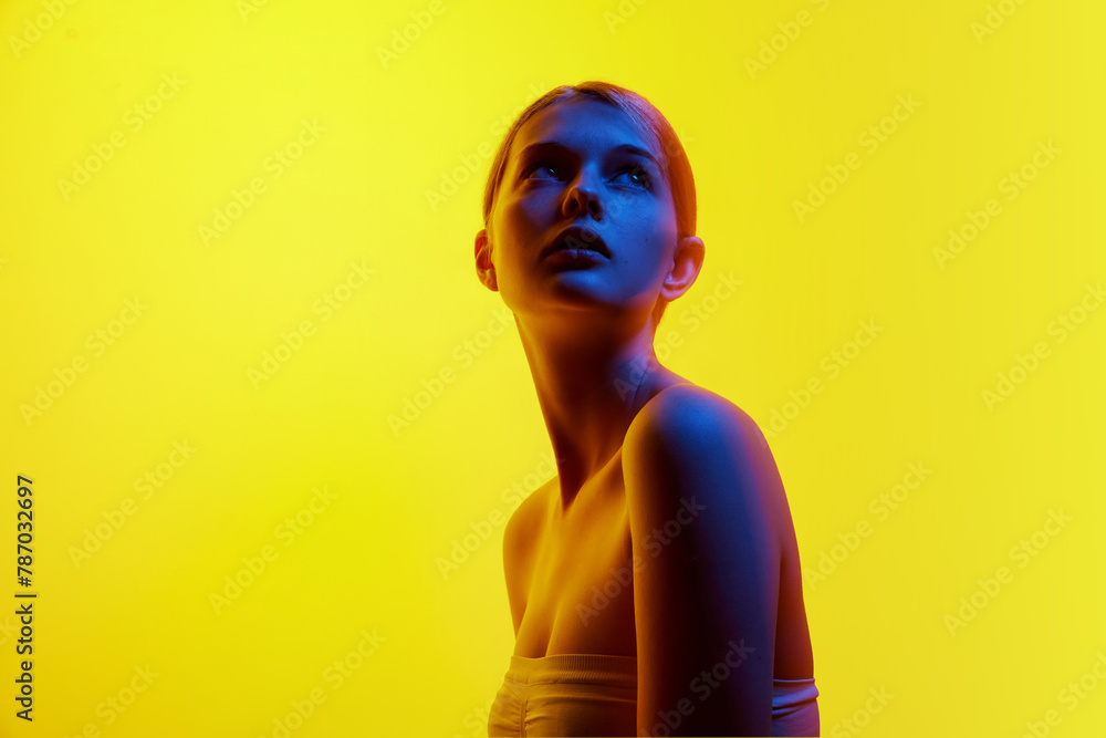 Portrait of young attractive woman in top posing looking up in neon light against gradient studio background. Concept of natural beauty, organic cosmetic, spa procedures, face-care.