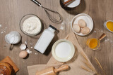 Flat lay essential ingredients for making cake or pastry with milk, egg, oil, flour, rolling pin, whisk random arranged on wooden kitchen table. Photo for advertising product of baking