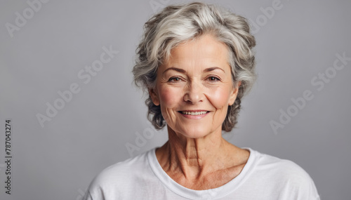 Beautiful mature woman with light grey background in a white t-shirt, studio shot 

