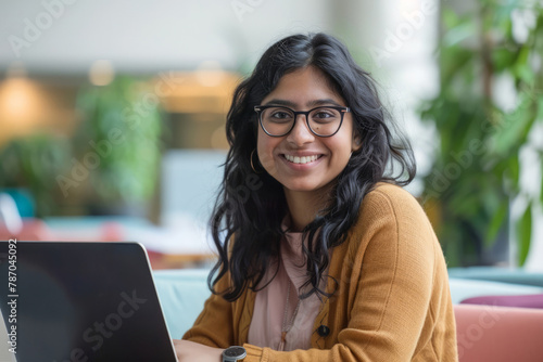 An optimistic Indian woman works on her laptop in a vibrant office setting, showcasing success and positivity.