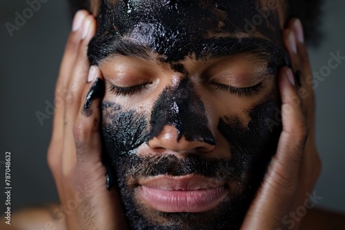 Close-up portrait of a man with eyes closed, applying a detoxifying charcoal mask on his face photo