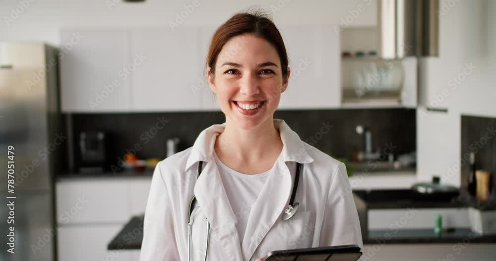Portrait of a happy brunette girl in a white doctors coat with a stethoscope on her shoulders and with a tablet in her hands near a modern kitchen in an apartment for a home examination Portrait of a happy brunette girl in a white doctors coat with a stethoscope on her shoulders and with a tablet in her hands near a modern kitchen in an apartment for a home examination