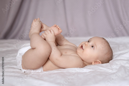 Young baby lying on white bed holding feet,  happy baby 6-7 months