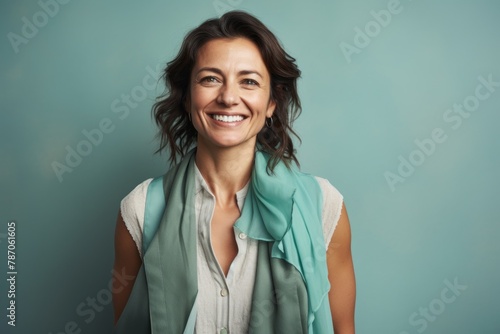 Portrait of a grinning woman in her 40s dressed in a polished vest over pastel teal background
