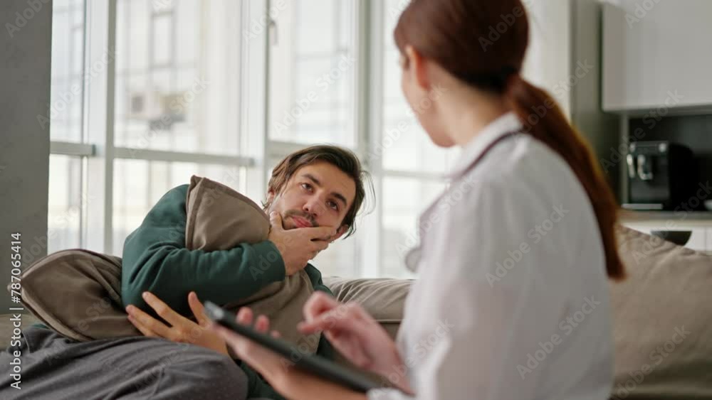 A brunette man with stubble in a green jacket tells a brunette girl doctor in a medical gown about his problems while sitting on the sofa and hugs in a modern apartment during a home examination A brunette man with stubble in a green jacket tells a brunette girl doctor in a medical gown about his problems while sitting on the sofa and hugs in a modern apartment during a home examination