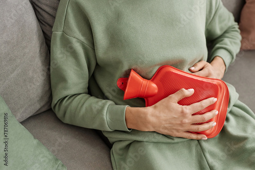 Close up of unrecognizable woman holding red hot water bottle to stomach suffering from period cramps copy space