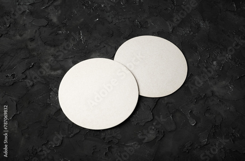 Two blank white beer coasters on black plaster background. Selective focus.
