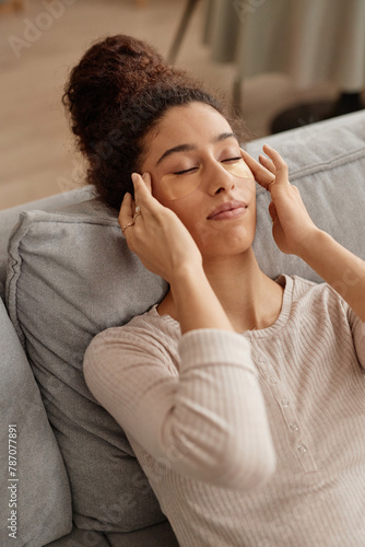 Vertical high angle portrait of young woman enjoying self care at home and doing face massage