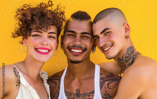 Grupo multirracial de tres jovenes posando sonrientes con ropa informal y tatuajes sobre fondo de color amarillo. Concepto colectivo lgtbiq+, dia del orgullo, dia contra la homofobia photo