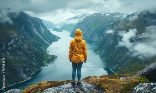 Portrait of a woman in a yellow raincoat standing from her back on a troll's tongue high in the mountains of Norway against the background of fjords photo