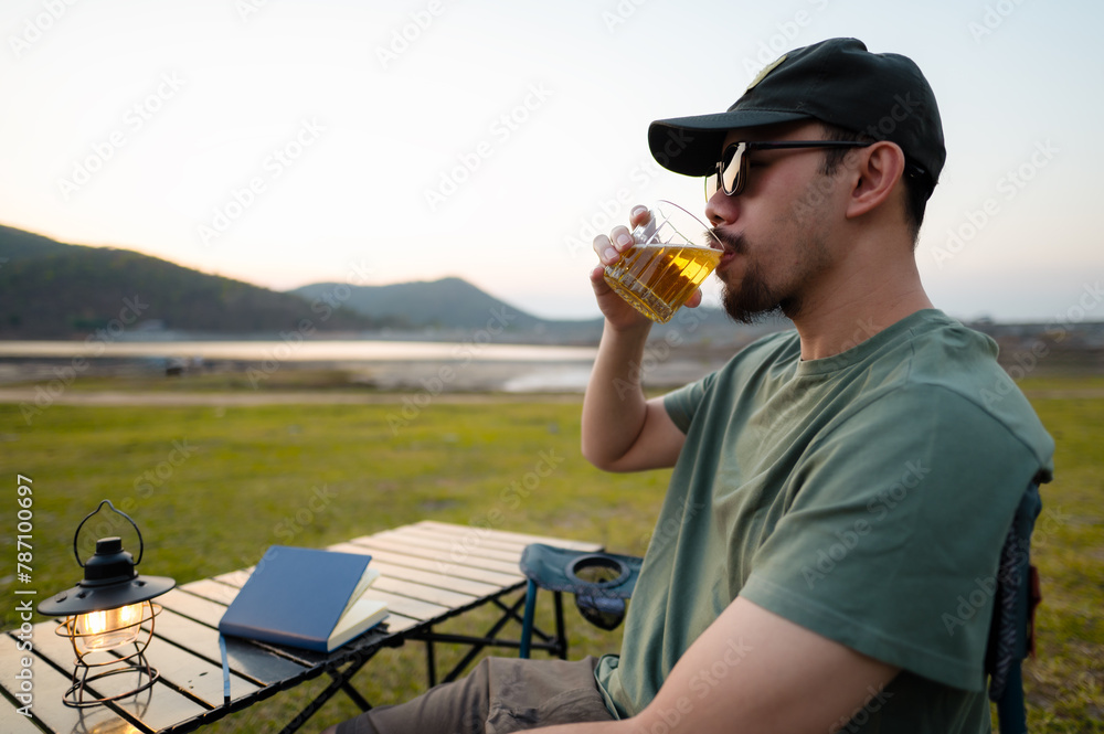 A relaxed man enjoys a peaceful moment sipping tea by a serene lakeside as the evening sets in.