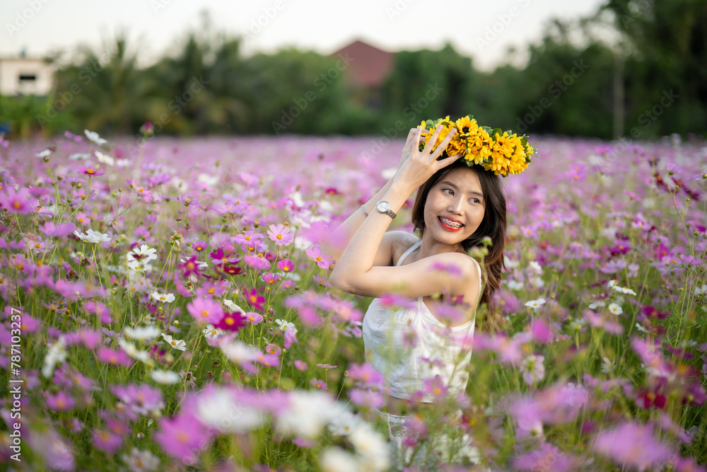 Fototapeta premium Young woman with floral crown smelling flowers in a vibrant field during sunset.