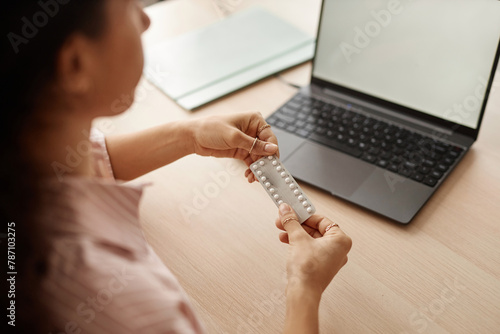 Close up of unrecognizable young woman holding blister of birth control pills and researching female health questions online copy space