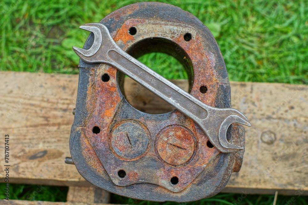 one part of a rusty old mechanical iron with an engine cylinder from a retro motorcycle lies with a wrench on wooden boards during the day on the street one part of a rusty old mechanical iron with an engine cylinder from a retro motorcycle lies with a wrench on wooden boards during the day on the street