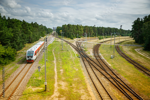 Fototapeta Naklejka Na Ścianę i Meble -  A modern passenger train moving along a railway track amidst a green landscape, in Klaipeda, Lithuania