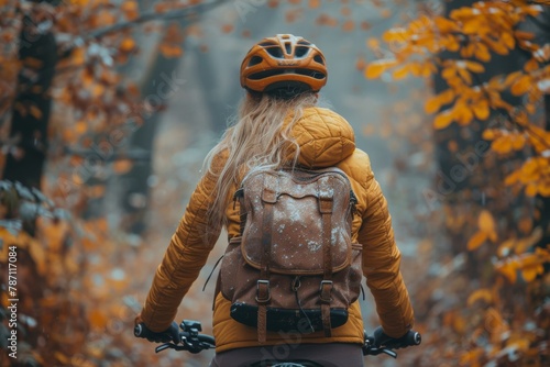 A cyclist with a yellow helmet and leather backpack traverses a mist-covered forest path, inviting adventure amidst fall beauty