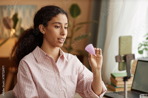 Portrait of multiracial young woman holding menstrual cup and recording videos via smartphone