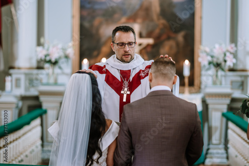 Fotografie Valmiera, Latvia- July 28, 2024 - A priest with a stole blesses a bride and groom during their wedding ceremony in a church