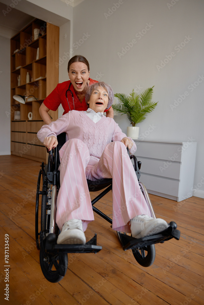 Crazy woman caregiver riding fast elderly woman patient on wheelchair - obrazy, fototapety, plakaty 