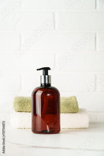Soap bottle and towel stack on white bathroom background.