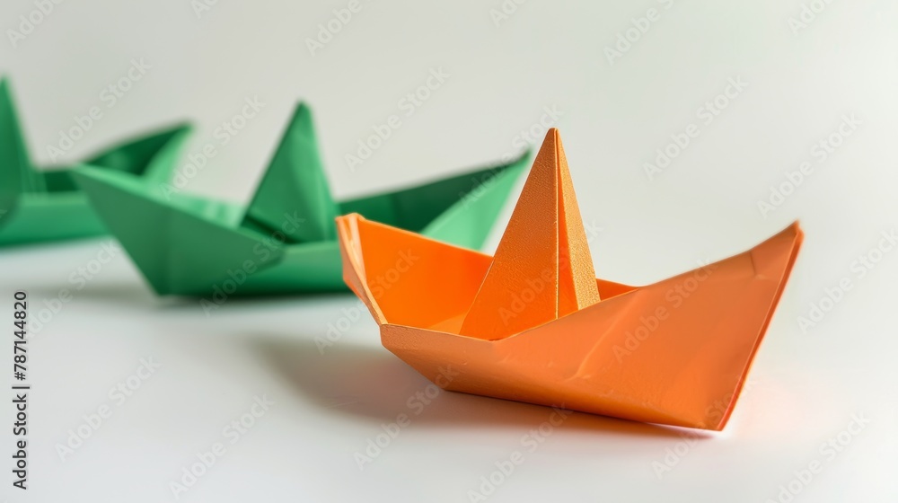 On white background, an orange paper boat leads a group of green paper boats. It represents leadership, individuality, and uniqueness. On white background, an orange paper boat leads a group of green paper boats. It represents leadership, individuality, and uniqueness.