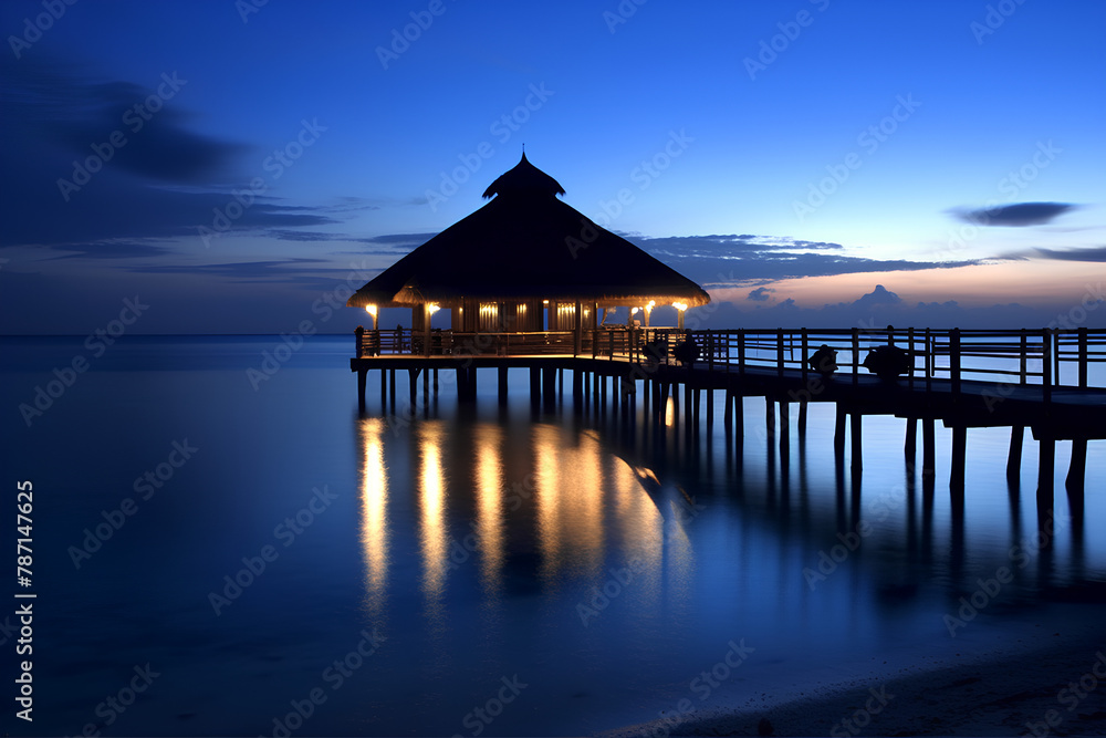 Sunset on the pier with the thatched roof, getting darker on the sea, beautiful blue and yellow colors.