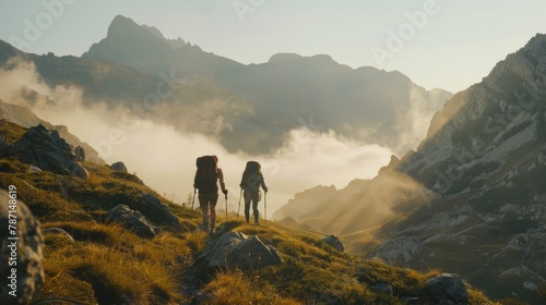 Two hikers walking on mountain trail at dawn with misty landscape.