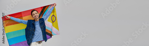 jolly appealing gay man in vibrant casual attire holding rainbow flag and smiling at camera, banner