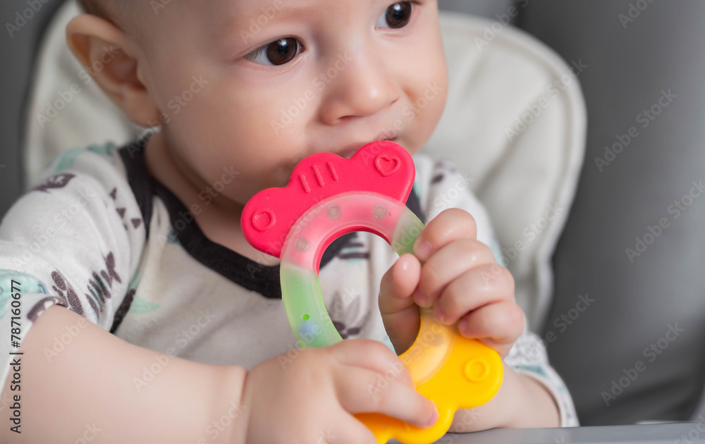 Portrait of a child who bites a multi-colored toy massager for teething in children. Help with teething. Itching of gums and salivation, dental accessory. Portrait of a child who bites a multi-colored toy massager for teething in children. Help with teething. Itching of gums and salivation, dental accessory.