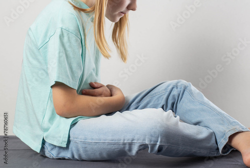 A little girl of seven years old sits and holds her sore stomach. The concept of improper digestion due to the pancreas, the production of enzymes. Pancreatitis and splenomegaly. Copy space for text photo