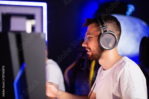 Bristly adult gamer in headset playing PC video game at computer club with team cyber sport tournament. E-sport championship. Player in headphones. Multiplayer online real-time strategy shooter